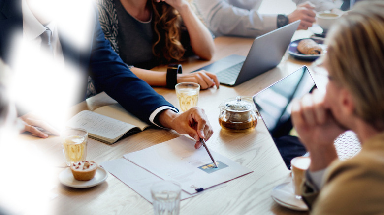 ऑफिसमधील लोक टेबलाभोवती काम करत आहेत.