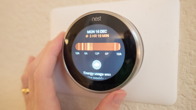 स्मार्ट नेस्ट थरोमोस्टॅट समायोजित करणाऱ्या हाताचा क्लोज-अप