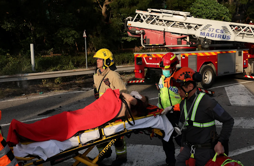 अपघातानंतर आपत्कालीन कर्मचारी जखमी व्यक्तीला सुरक्षित स्थळी नेत आहेत.