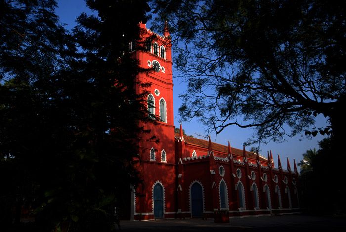 यात हे समाविष्ट असू शकते: त्याच्या बाजूला घड्याळ असलेली उंच लाल इमारत आणि अग्रभागी झाडे