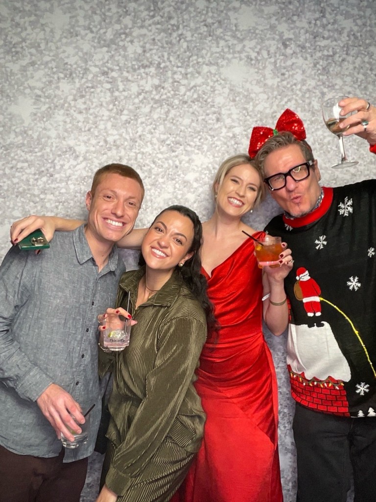 हॉलिडे फॅशन स्टोरीसाठी कपडे घातलेले चार लोक फोटोसाठी पोज देत आहेत.