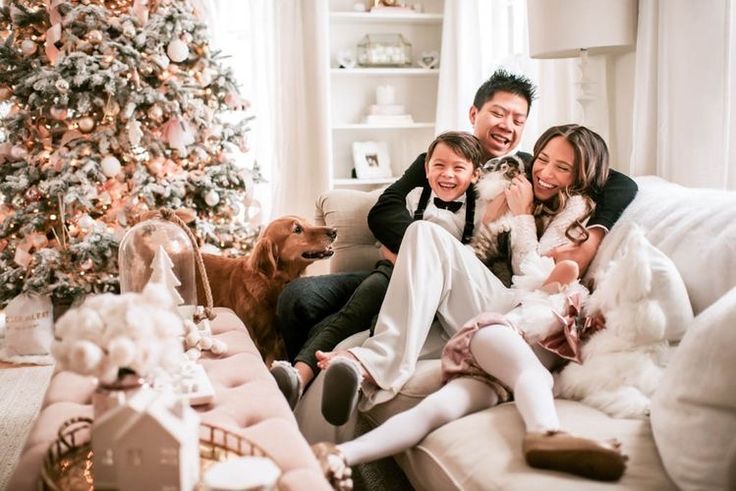 यात हे असू शकते: ख्रिसमस ट्रीसमोर पलंगावर बसलेले कुटुंब