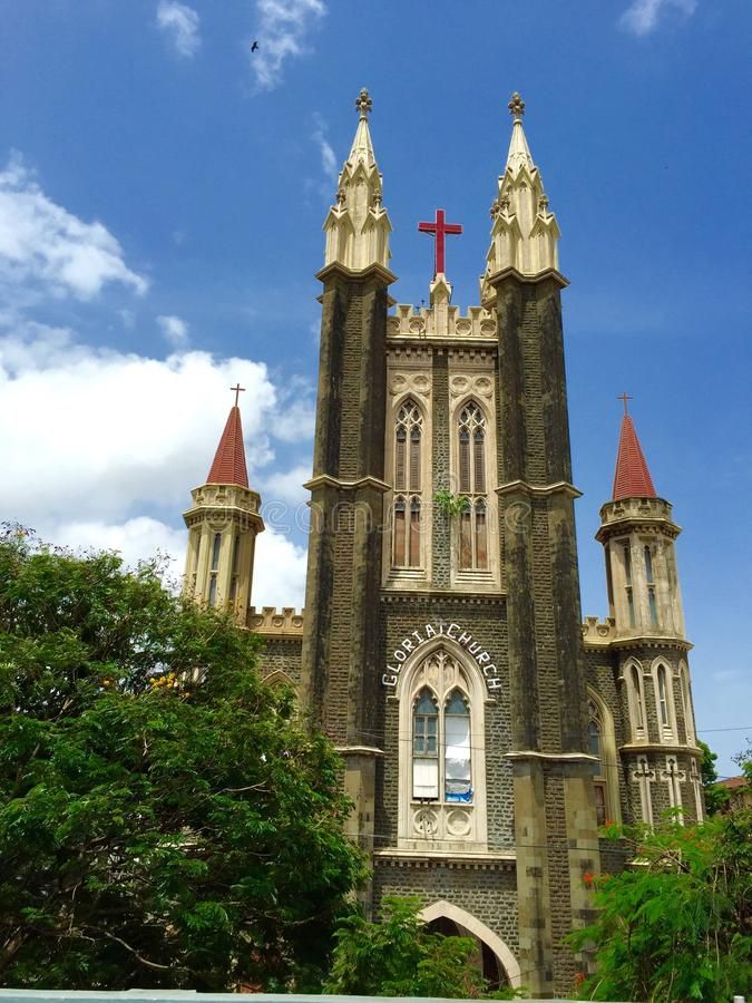 यात याचा समावेश असू शकतो: दोन टॉवर आणि वर क्रॉस असलेले जुने चर्च हिरवाईने वेढलेले आहे