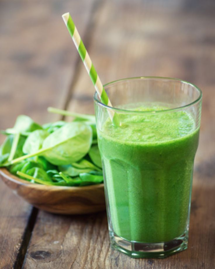 यात हे असू शकते: एका काचेमध्ये हिरवी स्मूदी, ज्याच्या शेजारी लाकडी टेबलावर पेंढा आहे