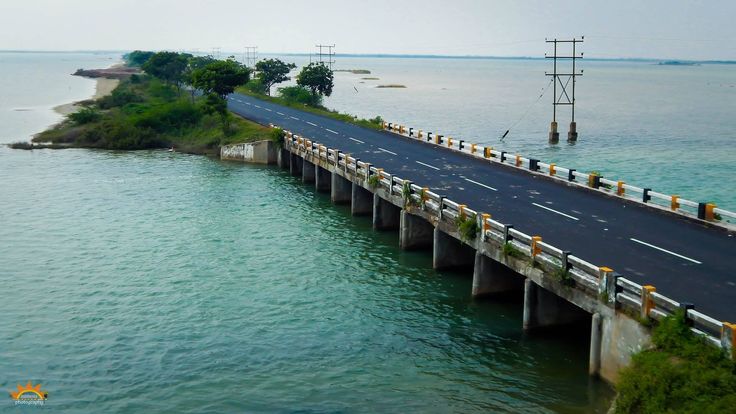 यात हे असू शकते: एका बाजूला गाड्या आणि दुसऱ्या बाजूला पाणी असलेल्या समुद्रावरील पुलाचे हवाई दृश्य