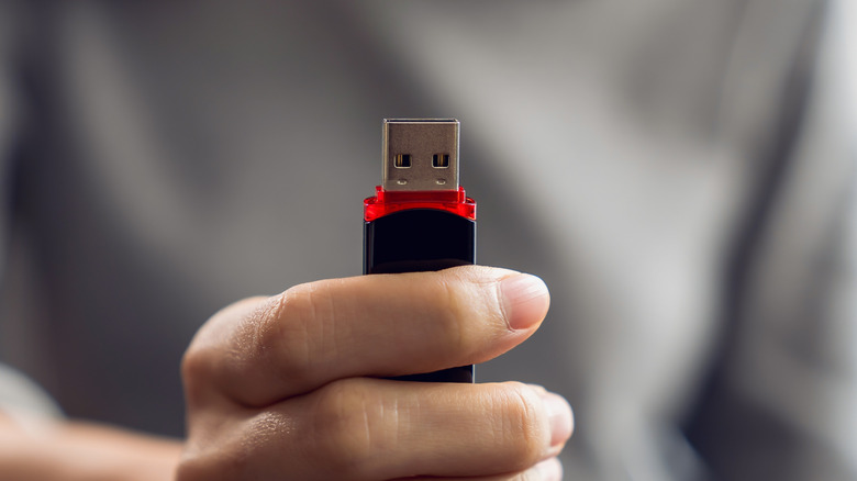 USB थंब ड्राईव्ह धरलेल्या व्यक्तीचा क्लोज-अप.