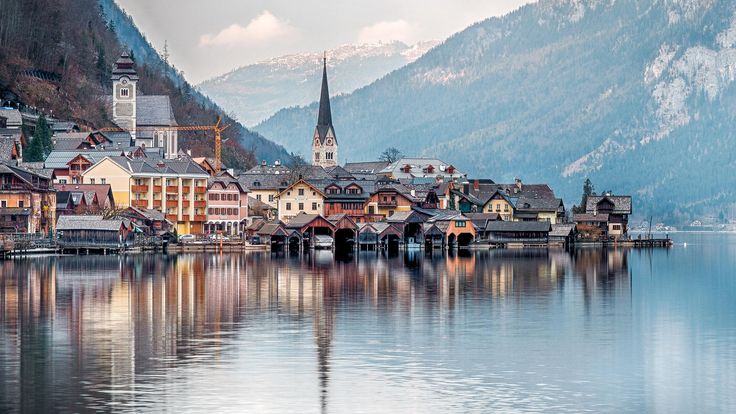 यामध्ये हे असू शकते: पार्श्वभूमीत पर्वत असलेले तलावाच्या किनाऱ्यावर असलेले शहर