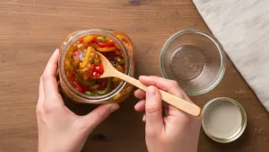 लाकडी चमच्याने काचेच्या बरणीत भोपळी मिरची मुरब्बा