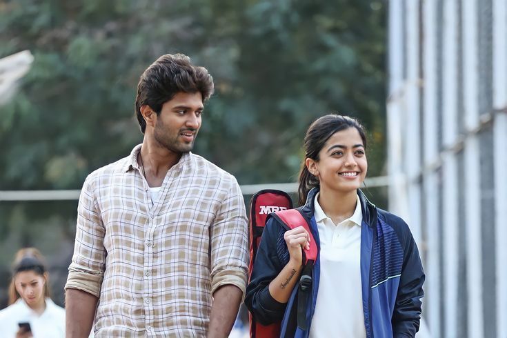 यात हे असू शकते: खांद्यावर बॅकपॅक घेऊन एकमेकांच्या शेजारी उभे असलेले एक पुरुष आणि स्त्री हसत आहेत