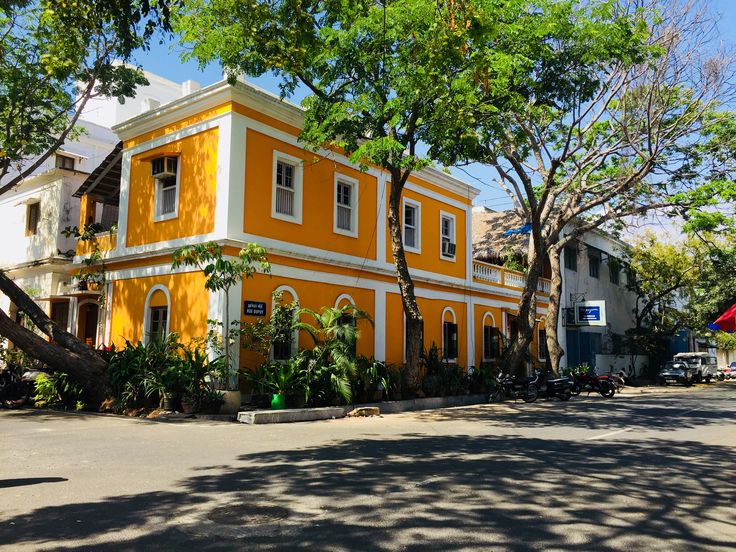 यात हे असू शकते: रस्त्याच्या कडेला काही झाडांच्या शेजारी बसलेली केशरी आणि पांढरी इमारत