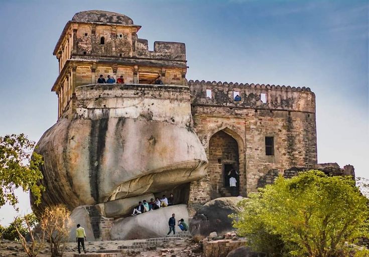 यामध्ये हे असू शकते: लोक किल्ल्यासारख्या संरचनेच्या समोरील खडकाच्या वर उभे आहेत