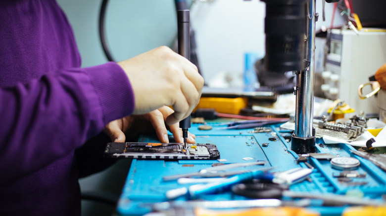 स्क्रू ड्रायव्हरसह स्मार्टफोनचे पृथक्करण करणारे तंत्रज्ञ