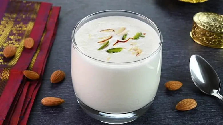 चिरलेल्या शेंगदाण्यांनी सजलेली गोड लस्सी, बाजूला बदाम टाकून ग्लासमध्ये सर्व्ह केली जाते.