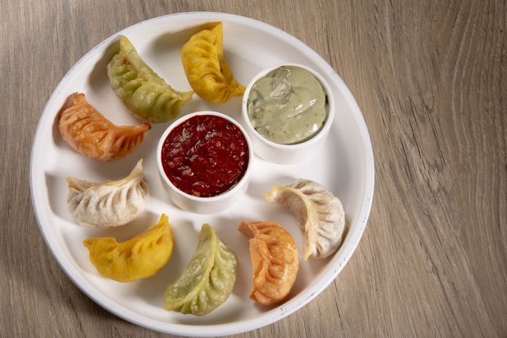 यात हे असू शकते: लाकडी टेबलाच्या वर डंपलिंग आणि सॉससह पांढरी प्लेट