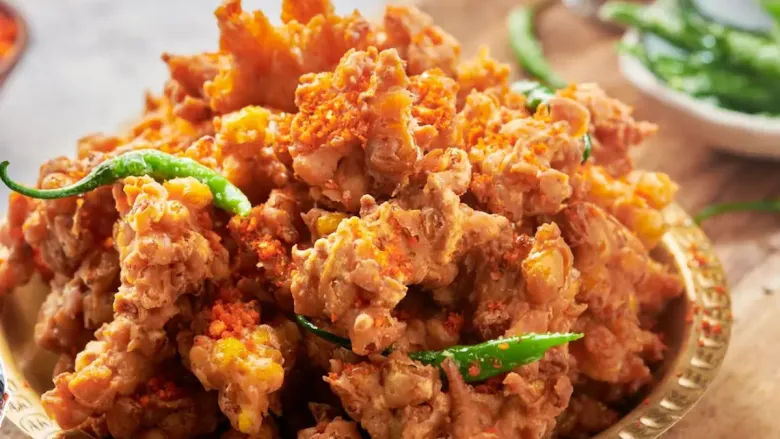 प्लेटमध्ये क्रिस्पी कॉर्न फ्रिटर हिरव्या मिरच्यांसोबत सर्व्ह केले जातात