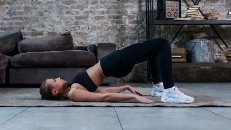 कूल्हे उचलून आणि जमिनीवर पाय ठेवून सेतू बंधनासन (ब्रिज पोझ) योग करत असलेली स्त्री.