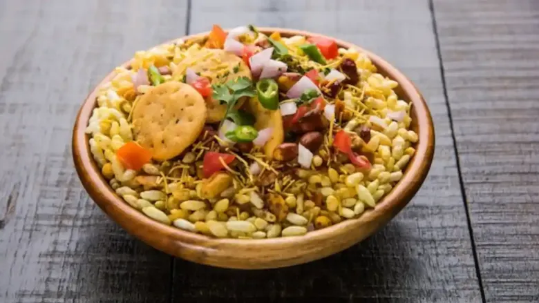 भेळ पुरी, शेव, चिरलेले कांदे, टोमॅटो आणि कोथिंबीर यांनी बनवलेले लोकप्रिय भारतीय स्ट्रीट फूड, भेल पुरीने भरलेले लाकडी वाडगा, ज्यामध्ये सपाट कुरकुरीत पापड होते.