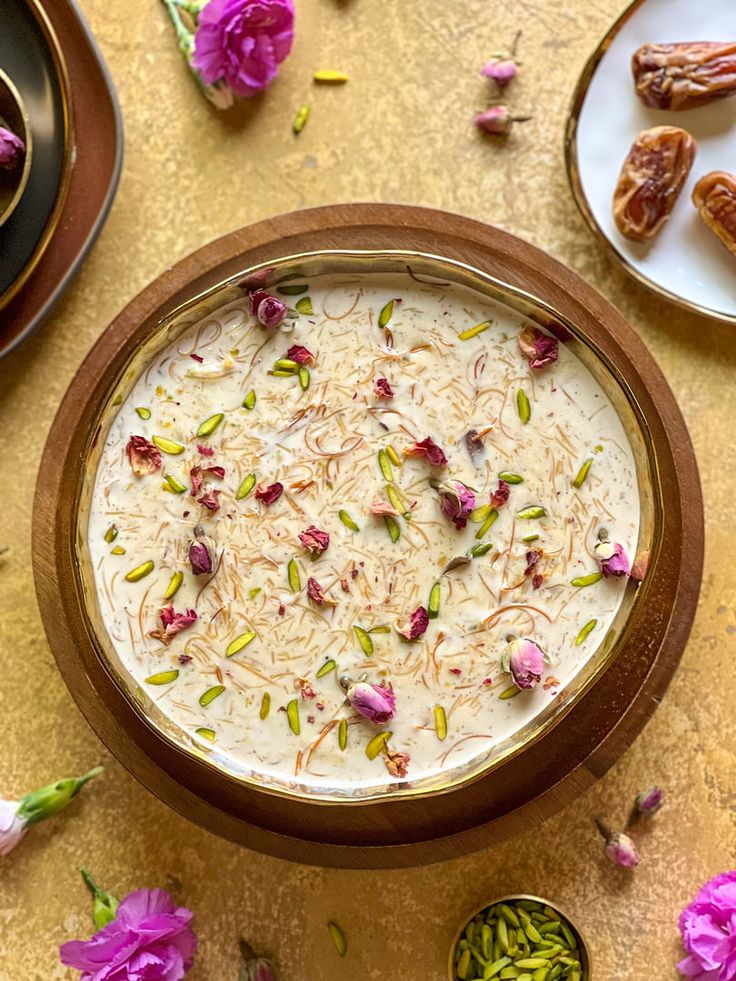 यात हे समाविष्ट असू शकते: इतर वाट्या आणि चमच्यांच्या शेजारी टेबलच्या वर बसलेला अन्नाने भरलेला वाडगा