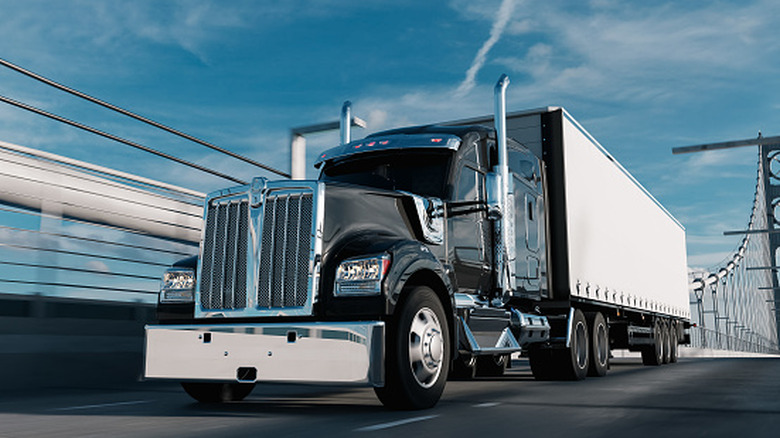 ब्रिज ओलांडून पांढरा मालवाहू कंटेनर आणणारा ठराविक अमेरिकन मोठा-रिग ट्रक, समोर-डावीकडे दृश्य