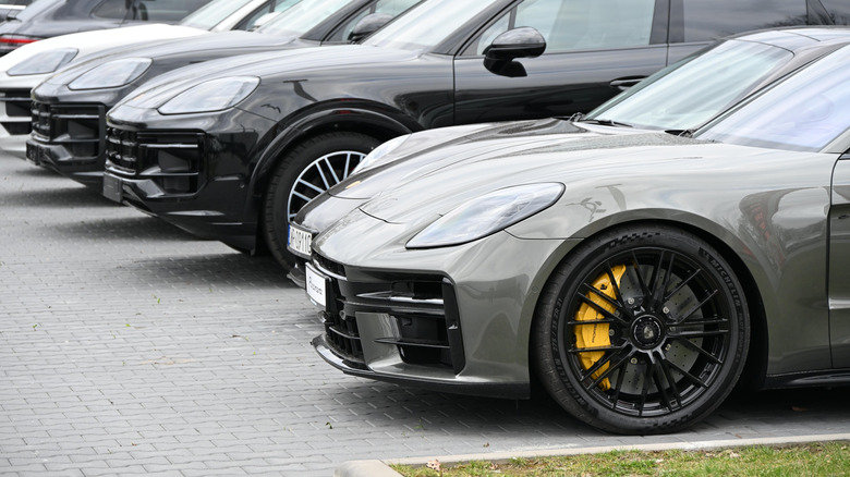 डीलर लॉटमध्ये नवीन पोर्श कार, अग्रभागी हिरवा Panamera आणि 911, पुढे विविध Cayennes