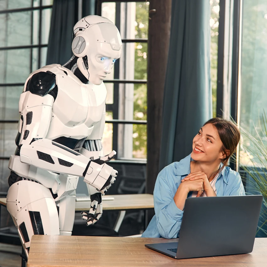 कार्यालयातील महिला कर्मचाऱ्याच्या संगणकाच्या स्क्रीनकडे पाहणारा कृत्रिम बुद्धिमत्ता असलेला रोबोट