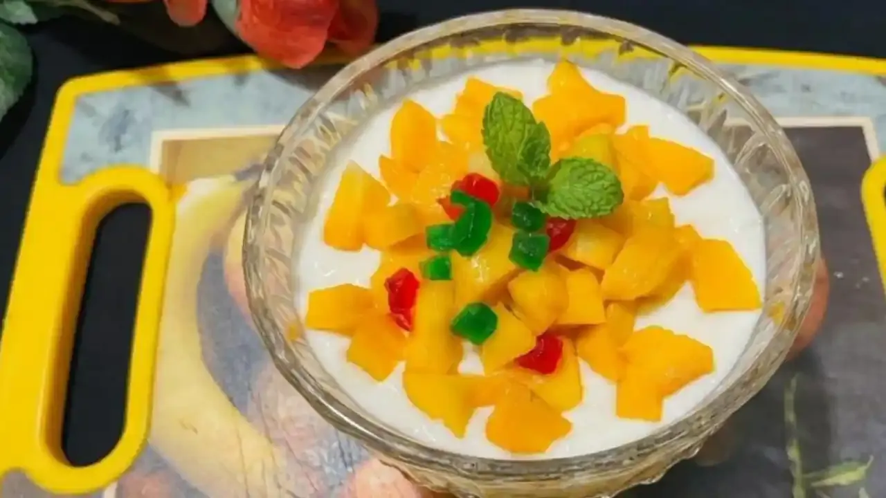 स्फटिकाच्या भांड्यात ताज्या फळांचे तुकडे, रंगीबेरंगी टुटी फ्रुटी आणि पुदिन्याची पाने असलेली स्वादिष्ट आंब्याची खीर.