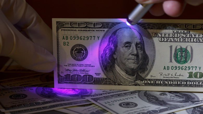 अतिनील प्रकाशासह $100 चे बिल तपासत आहे