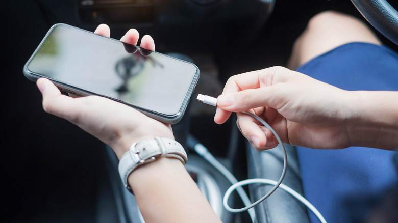 चार्जिंगसाठी USB केबल वापरून आणि Android Auto वापरून त्यांचा फोन कारशी जोडणारी व्यक्ती