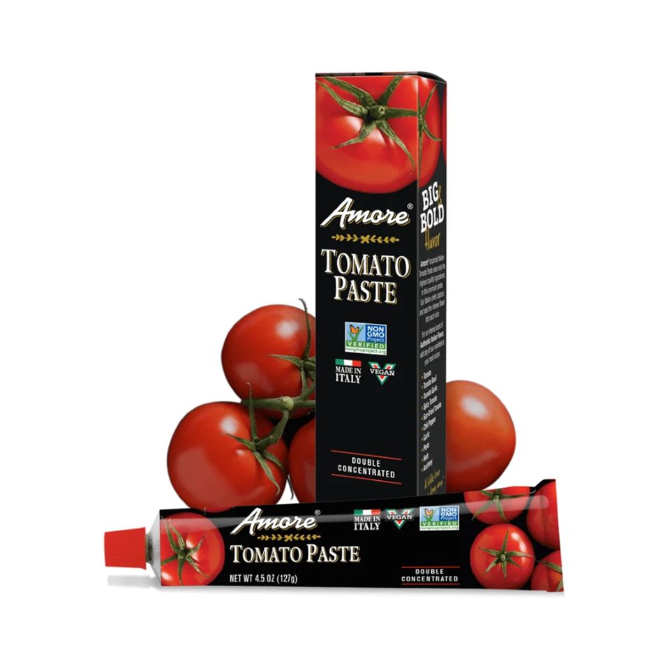 A tube and box of Amore Tomato Paste placed near fresh tomatoes